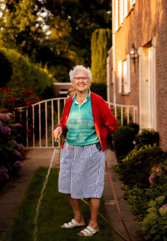 A cheerful elderly woman waters her lush garden on a sunny summer day.