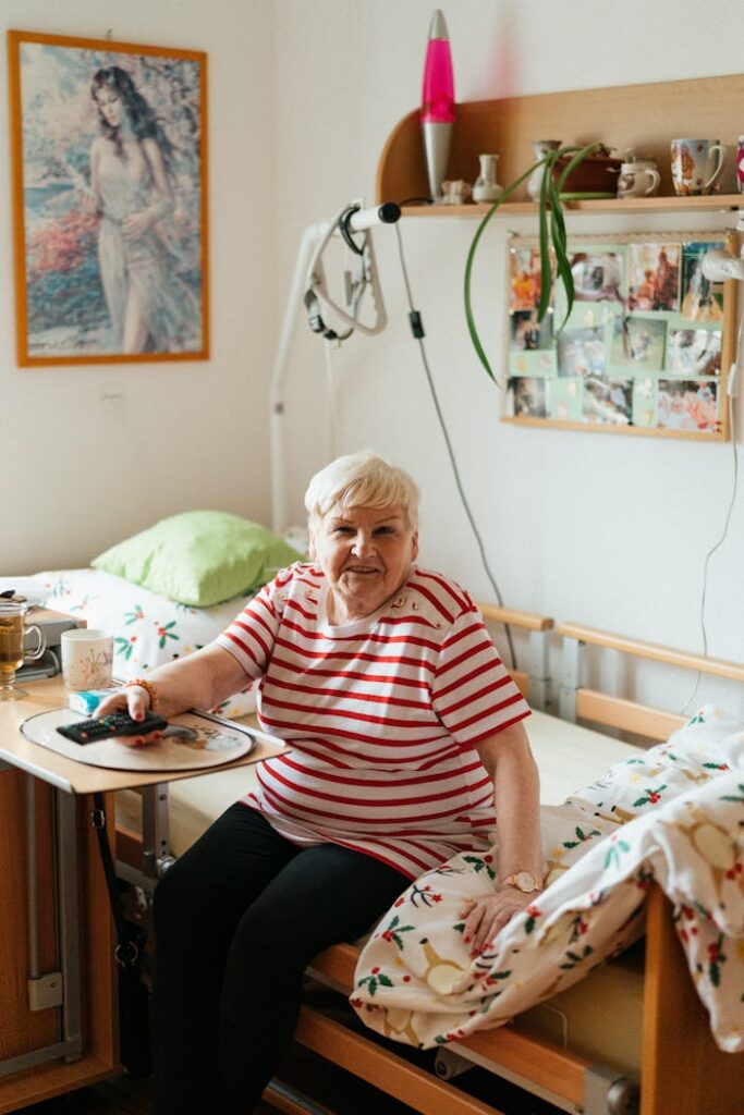 Elderly woman in a striped T-shirt smiling while sitting in her room, showcasing a cozy and warm atmosphere.