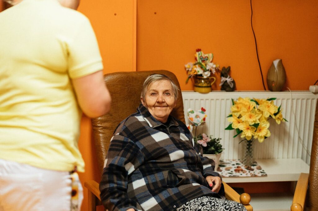 Crafting Captivating Headlines: Your awesome post title goes here A warm scene of a senior woman sitting in an armchair at a retirement home with a caretaker nearby.
