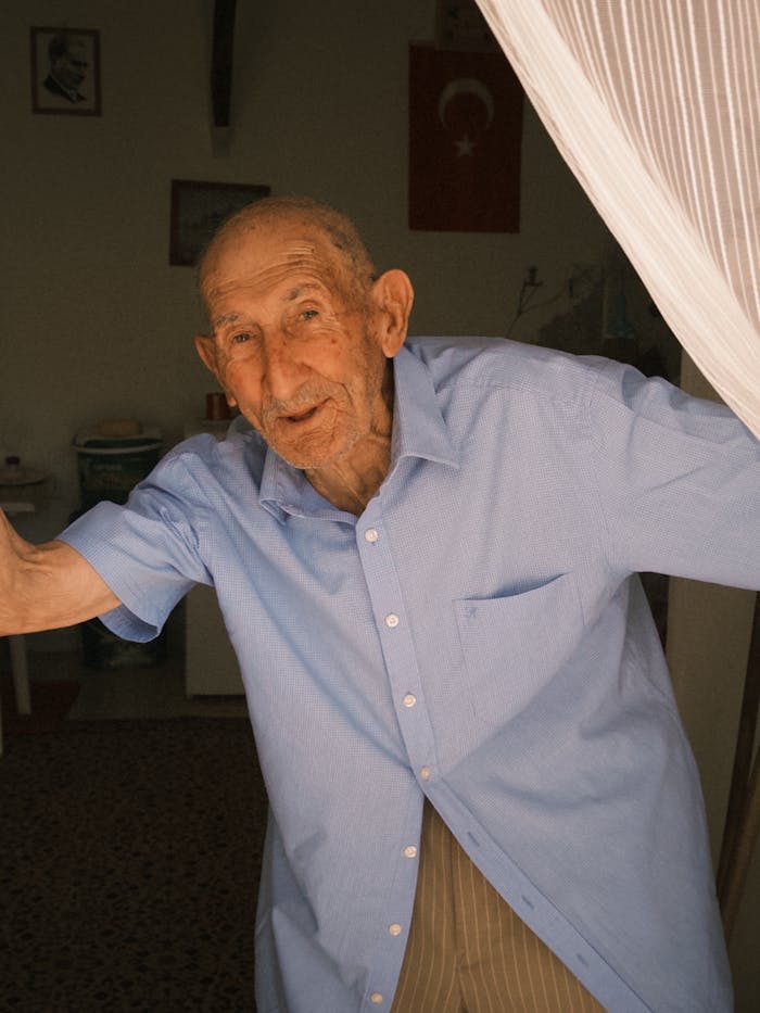 Senior man in casual attire warmly greeting from doorway indoors.