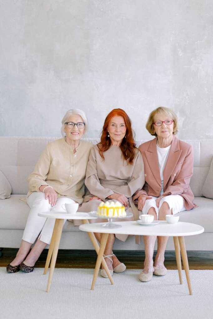 Elderly cheerful women in trendy outfit smiling and looking at camera at tables with tasty dessert and cups