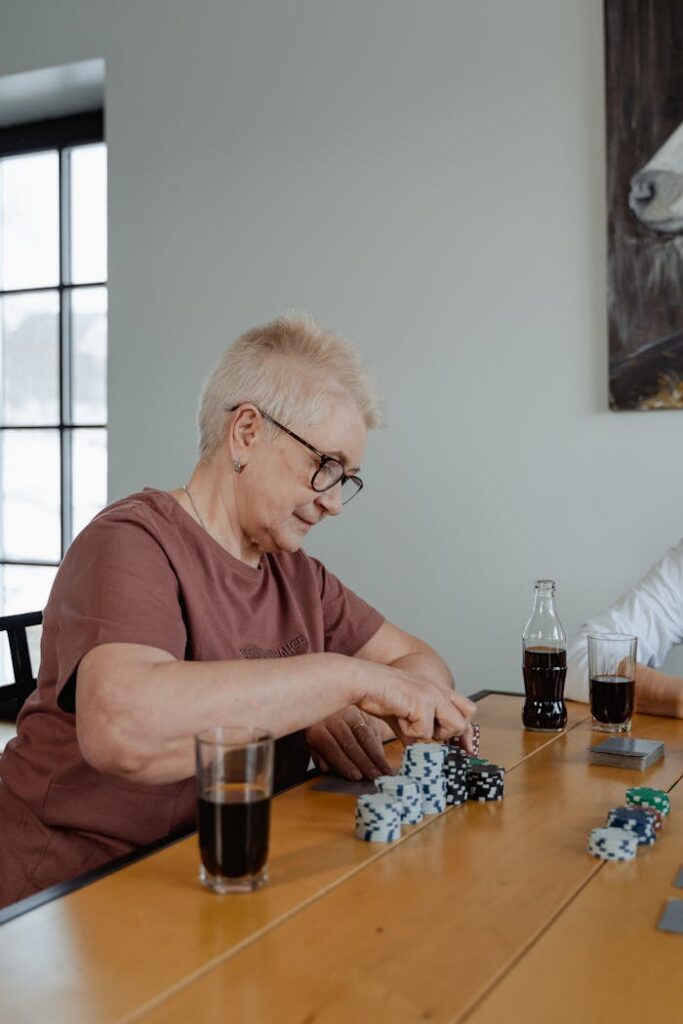 Senior woman enjoying a poker game at home, surrounded by drinks and chips.