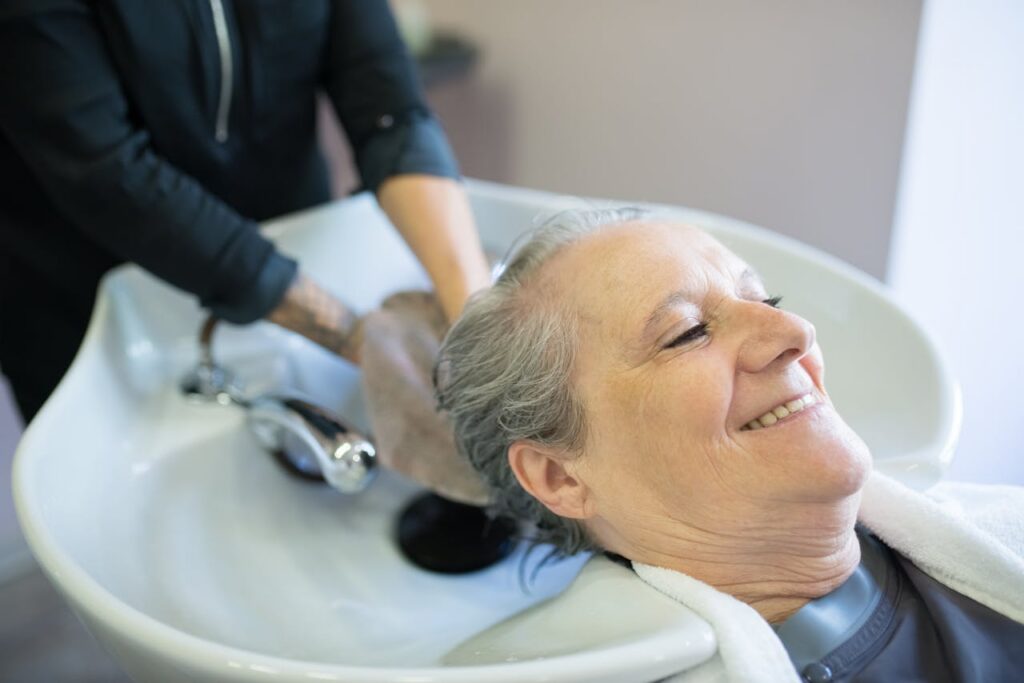 Mastering the First Impression: Your intriguing post title goes here Senior woman smiling while getting her hair washed at a salon sink by a hairdresser.